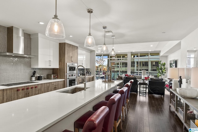 kitchen featuring white cabinetry, wall chimney range hood, backsplash, double oven, and pendant lighting