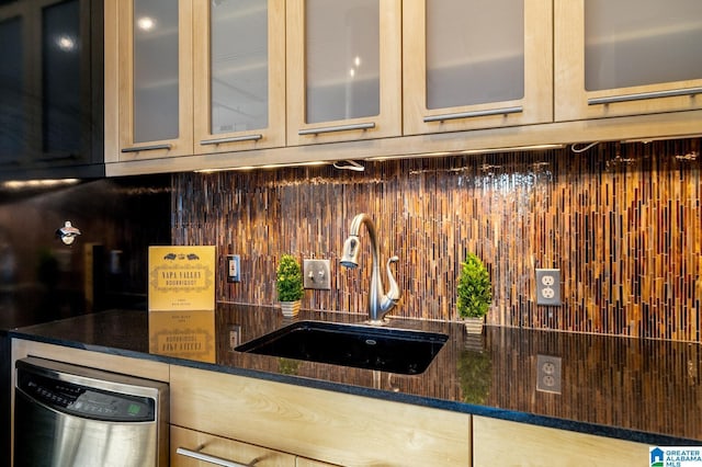 kitchen featuring backsplash, stainless steel dishwasher, dark stone counters, and sink