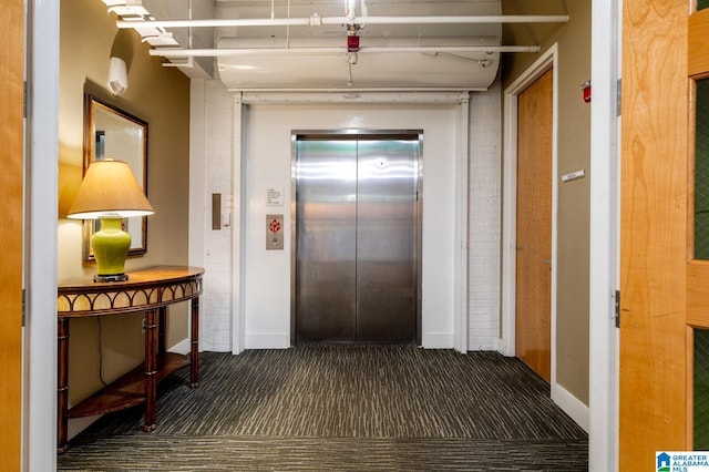 hall with dark colored carpet and elevator