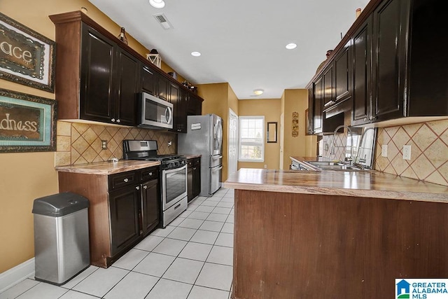 kitchen featuring appliances with stainless steel finishes, sink, light tile patterned floors, dark brown cabinetry, and kitchen peninsula