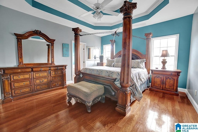 bedroom with ornate columns, a raised ceiling, ceiling fan, and light hardwood / wood-style floors