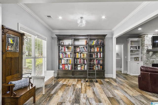 sitting room with a stone fireplace, crown molding, and hardwood / wood-style flooring