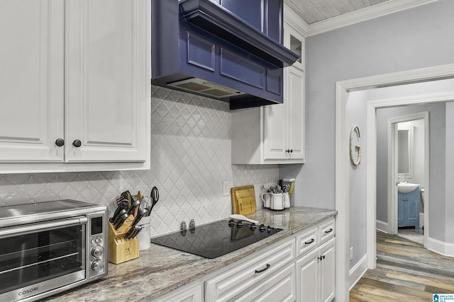 kitchen featuring white cabinetry, light stone counters, black electric cooktop, custom range hood, and ornamental molding