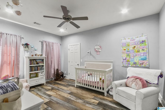 bedroom featuring dark hardwood / wood-style flooring, a nursery area, and ceiling fan