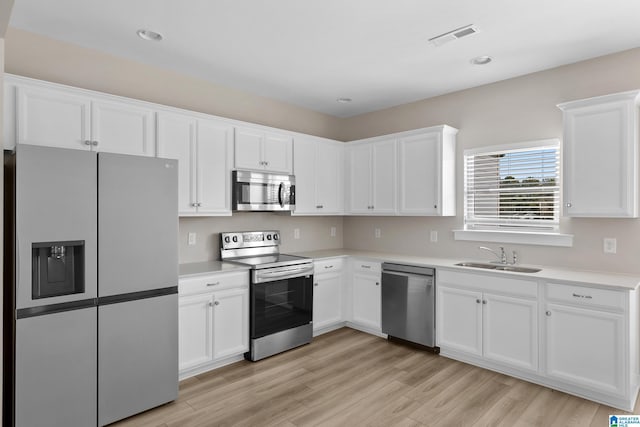 kitchen with stainless steel appliances, light hardwood / wood-style floors, white cabinetry, and sink