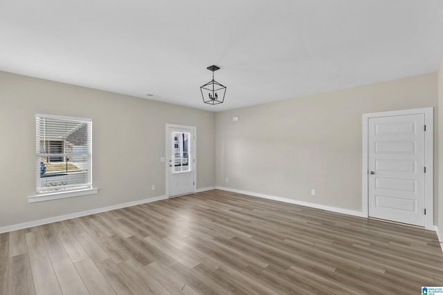 unfurnished room featuring a notable chandelier, a wealth of natural light, and light hardwood / wood-style floors