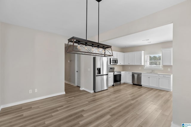 kitchen featuring decorative light fixtures, white cabinetry, stainless steel appliances, sink, and light wood-type flooring