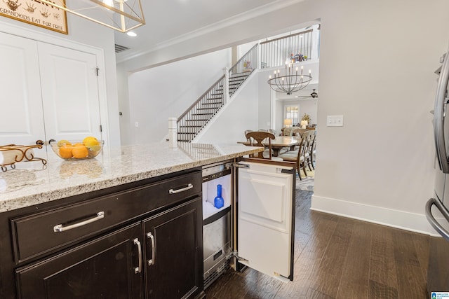 kitchen featuring dark wood-type flooring, light stone countertops, beverage cooler, crown molding, and ceiling fan with notable chandelier