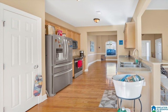 kitchen with light brown cabinetry, hanging light fixtures, sink, light wood-type flooring, and stainless steel appliances