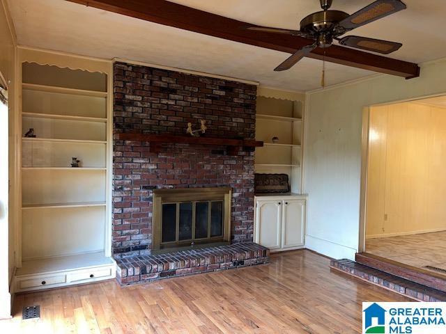 unfurnished living room featuring a brick fireplace, built in shelves, ceiling fan, light hardwood / wood-style flooring, and beamed ceiling