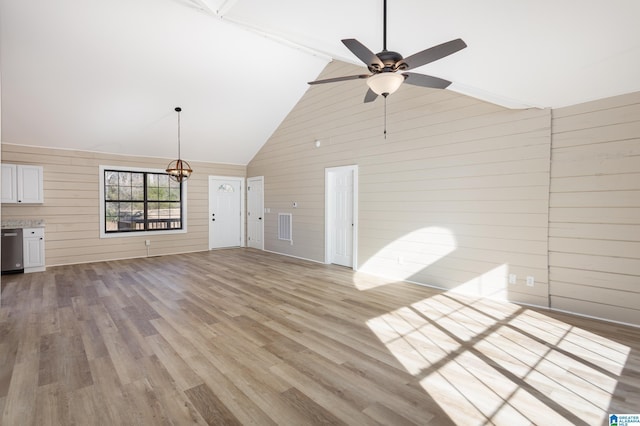 unfurnished living room with light wood-type flooring, high vaulted ceiling, ceiling fan, and wooden walls