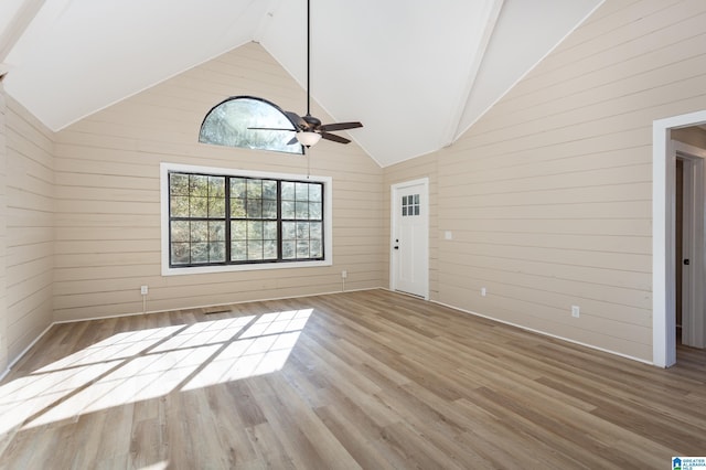 unfurnished living room featuring wooden walls, ceiling fan, high vaulted ceiling, and hardwood / wood-style flooring