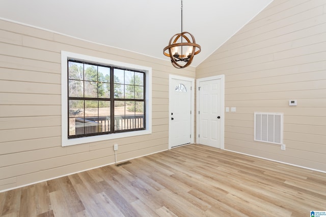 foyer featuring wooden walls, light hardwood / wood-style flooring, a chandelier, and vaulted ceiling