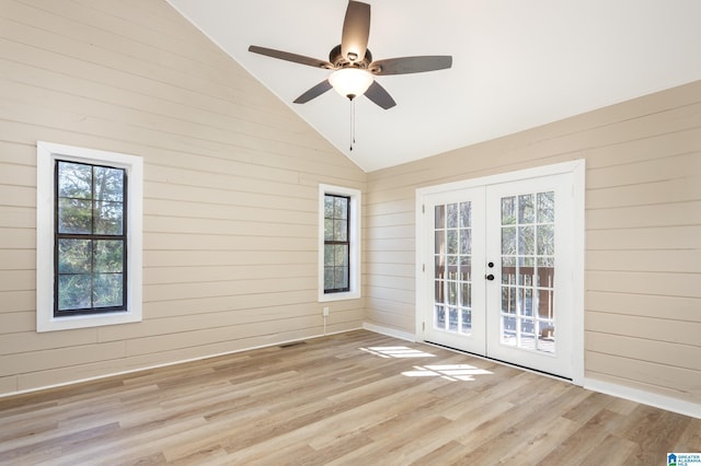 unfurnished room featuring ceiling fan, french doors, high vaulted ceiling, light hardwood / wood-style floors, and wooden walls