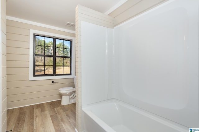 bathroom featuring wood walls, wood-type flooring, tub / shower combination, and toilet