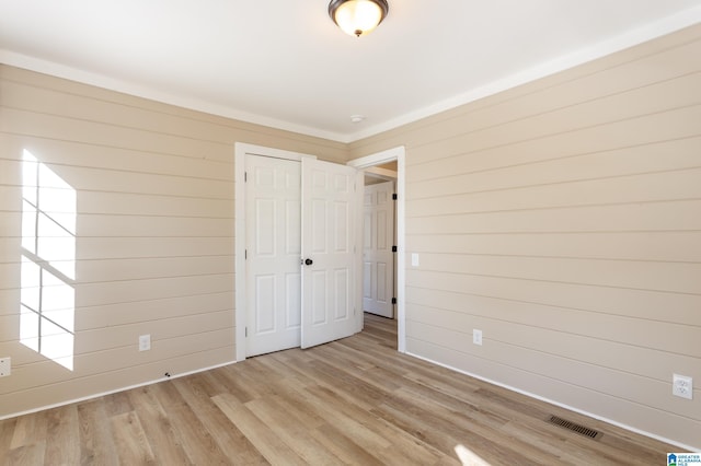 unfurnished bedroom with light wood-type flooring, a closet, and wooden walls