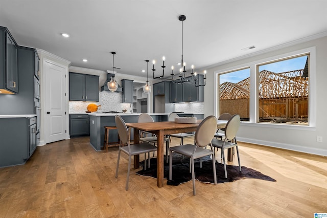 dining space with light wood-type flooring, a notable chandelier, and ornamental molding