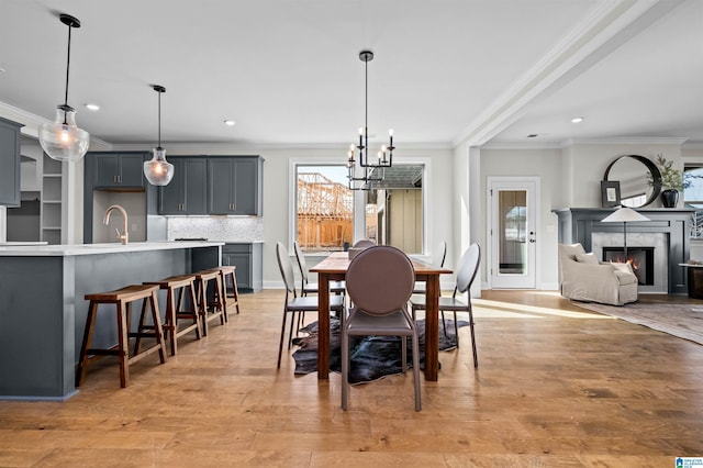 dining area featuring a tile fireplace, sink, an inviting chandelier, light hardwood / wood-style flooring, and ornamental molding