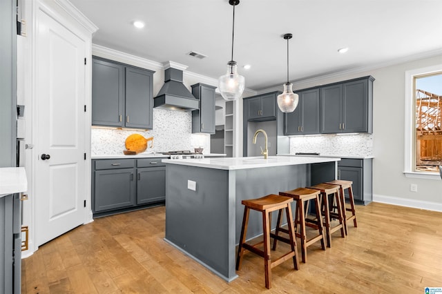 kitchen featuring an island with sink, pendant lighting, custom range hood, and ornamental molding