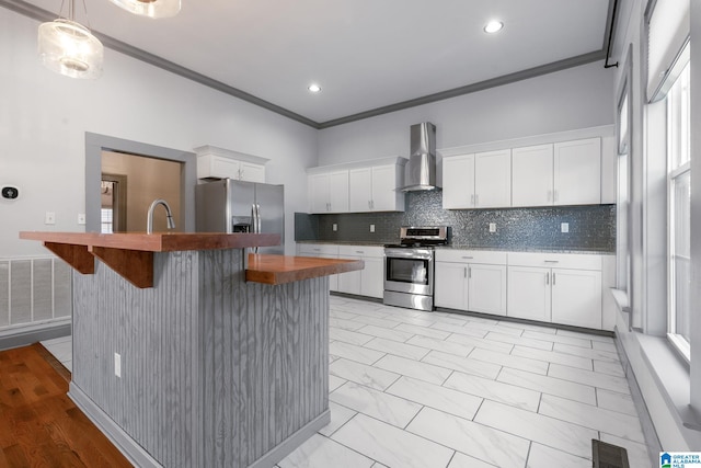 kitchen with stainless steel appliances, white cabinetry, wall chimney exhaust hood, a kitchen bar, and crown molding