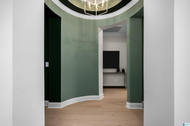 corridor featuring a tray ceiling, crown molding, light hardwood / wood-style flooring, and a chandelier