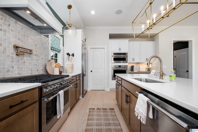 kitchen with high end appliances, premium range hood, sink, hanging light fixtures, and white cabinetry