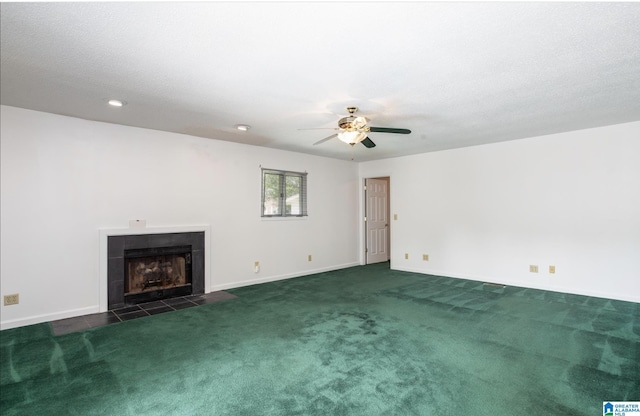 unfurnished living room featuring a tile fireplace, dark colored carpet, and ceiling fan