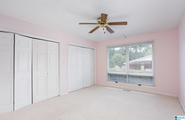 unfurnished bedroom with ceiling fan, light carpet, and two closets