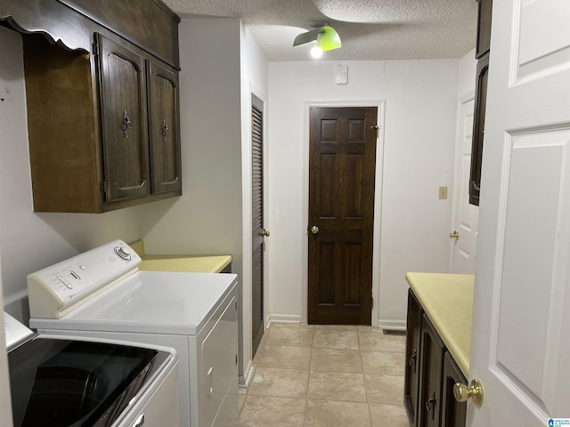 washroom featuring washing machine and clothes dryer, light tile patterned floors, cabinets, and a textured ceiling