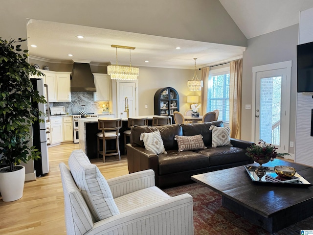 living room featuring ornamental molding, light hardwood / wood-style flooring, lofted ceiling, and an inviting chandelier