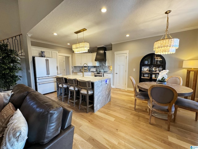 kitchen featuring pendant lighting, white cabinets, a kitchen island with sink, custom range hood, and high end fridge