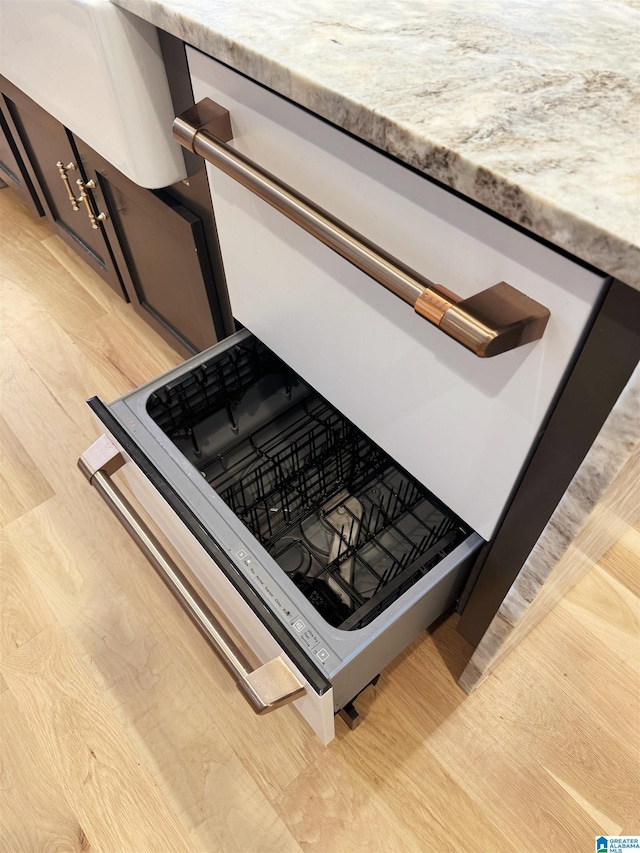 interior details with dishwasher, light stone counters, and light hardwood / wood-style floors