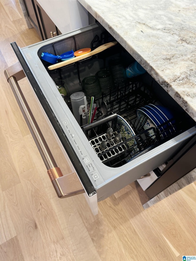 interior details with dishwasher, hardwood / wood-style flooring, and light stone countertops