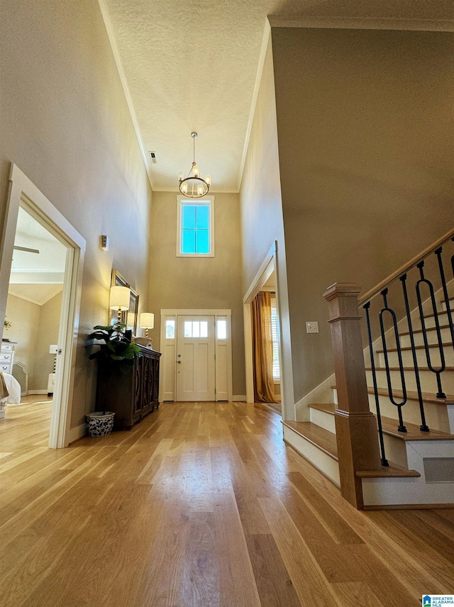 entrance foyer with a high ceiling, wood-type flooring, ornamental molding, and an inviting chandelier