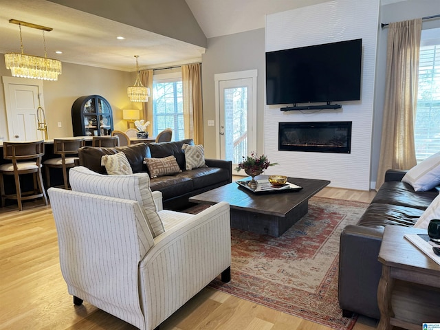 living room featuring light wood-type flooring, a chandelier, vaulted ceiling, and a large fireplace