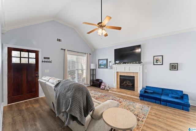 living room featuring ceiling fan, hardwood / wood-style flooring, ornamental molding, a tiled fireplace, and vaulted ceiling