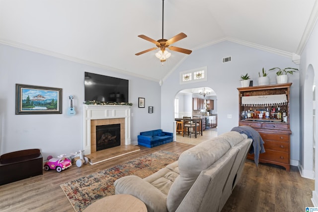 living room featuring wood-type flooring, crown molding, vaulted ceiling, ceiling fan, and a tiled fireplace