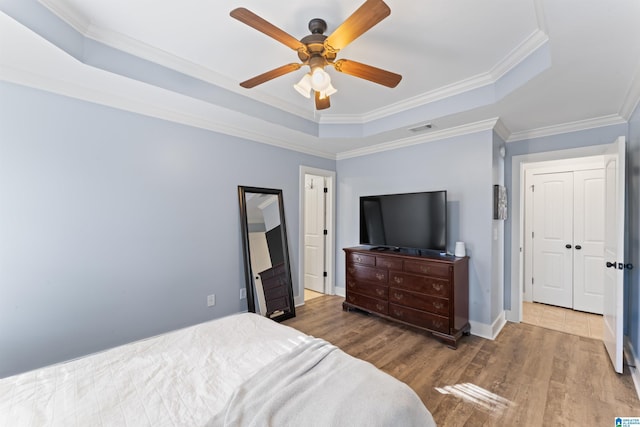 bedroom with hardwood / wood-style flooring, a closet, ornamental molding, a raised ceiling, and ceiling fan