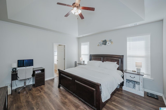 bedroom with a raised ceiling, dark hardwood / wood-style floors, ensuite bath, and ceiling fan