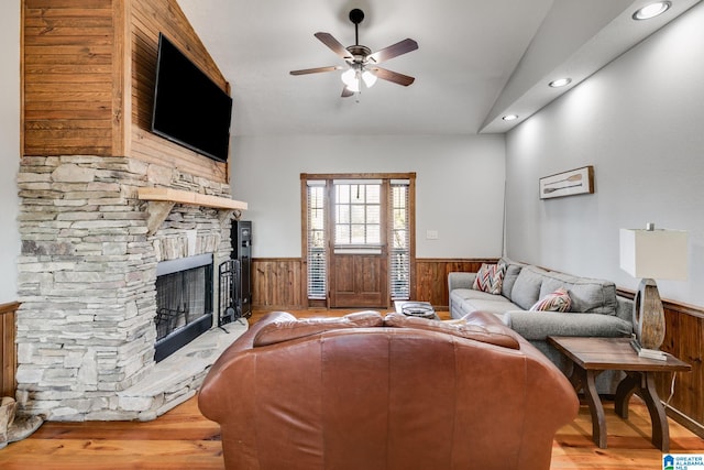 living room with light hardwood / wood-style floors, a stone fireplace, ceiling fan, and lofted ceiling