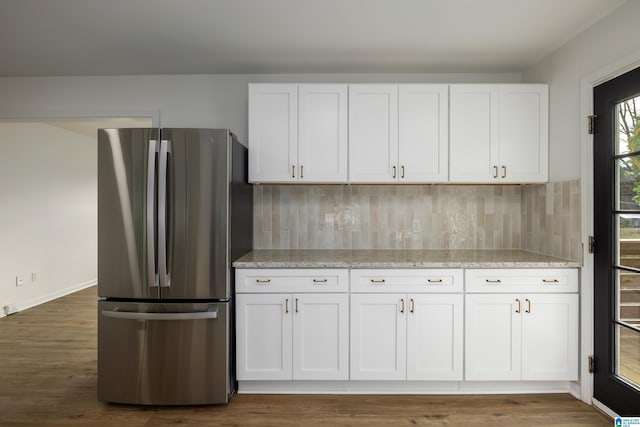 kitchen featuring light stone countertops, backsplash, white cabinetry, and stainless steel refrigerator