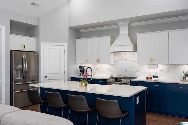 kitchen with white cabinets, appliances with stainless steel finishes, a center island with sink, and custom range hood