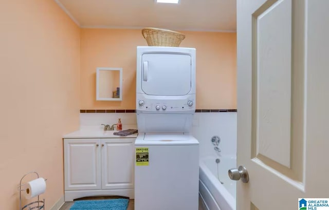 clothes washing area with stacked washer / drying machine and cabinets