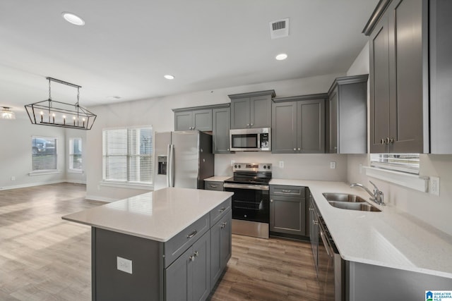 kitchen with sink, decorative light fixtures, gray cabinets, a kitchen island, and appliances with stainless steel finishes