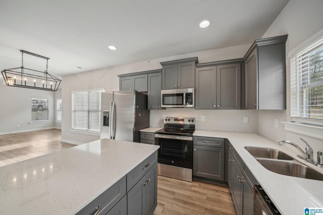 kitchen featuring light stone countertops, sink, light hardwood / wood-style floors, decorative light fixtures, and appliances with stainless steel finishes