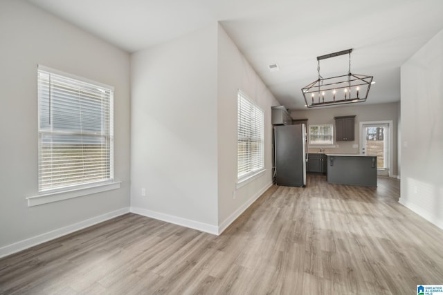 interior space with light wood-type flooring, an inviting chandelier, decorative light fixtures, and stainless steel refrigerator