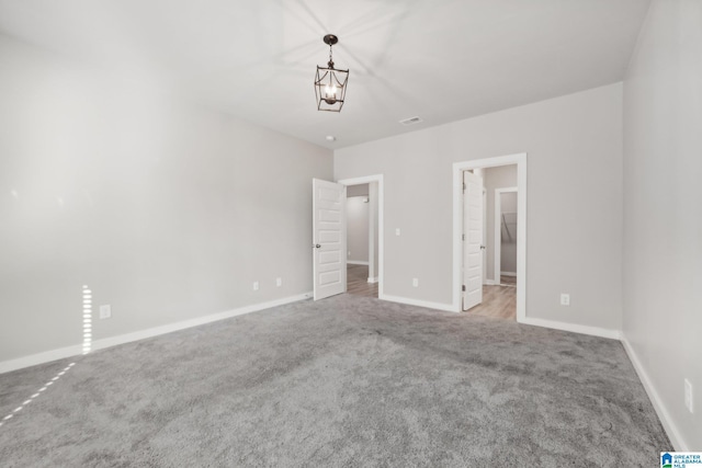 unfurnished bedroom featuring a walk in closet, light colored carpet, and an inviting chandelier