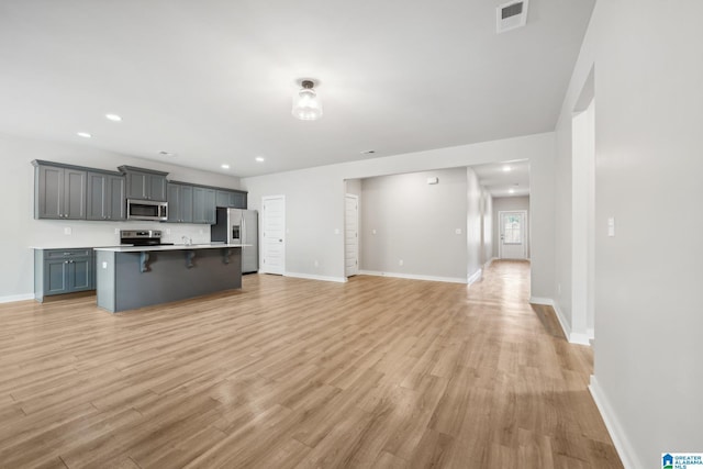 kitchen featuring gray cabinetry, a kitchen breakfast bar, light hardwood / wood-style floors, a center island with sink, and appliances with stainless steel finishes