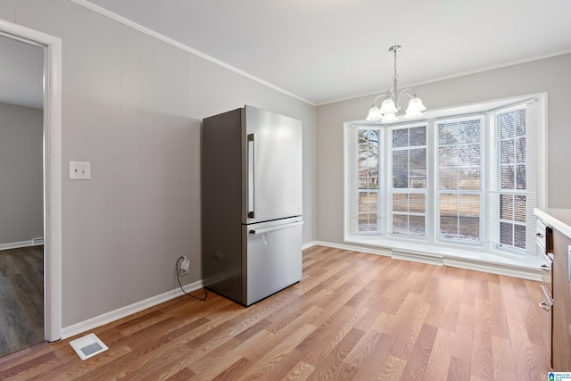 unfurnished dining area featuring light wood-type flooring, crown molding, and a chandelier