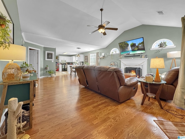 living room with vaulted ceiling, light wood-type flooring, ceiling fan, and ornamental molding